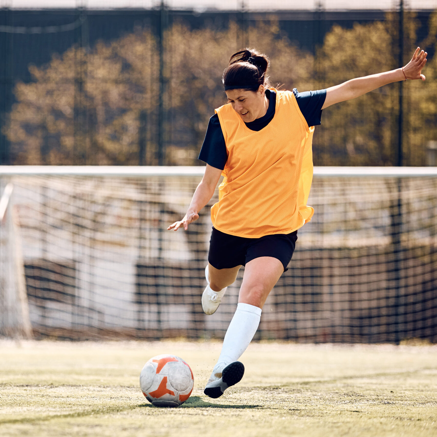 Roba esportiva Jugadora de futbol xutant una pilota portant roba de Logigràfic, marcatge i estampació de tèxtils i disseny gràfic personalitzat.